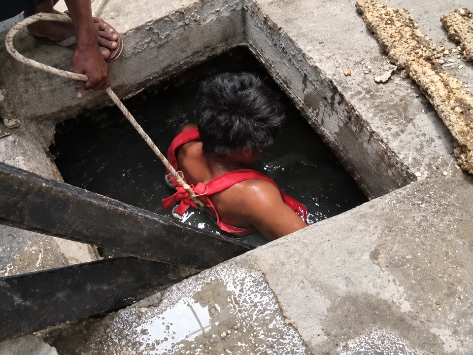 Worker carrying out manual cleaning inside a concrete septic tank